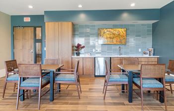 A dining area with tables and chairs and a kitchen in the background